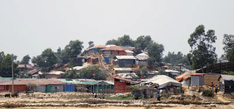 Shelters and steps on a hill in a Cox's Bazar camp, seen from a distance under a pale sky